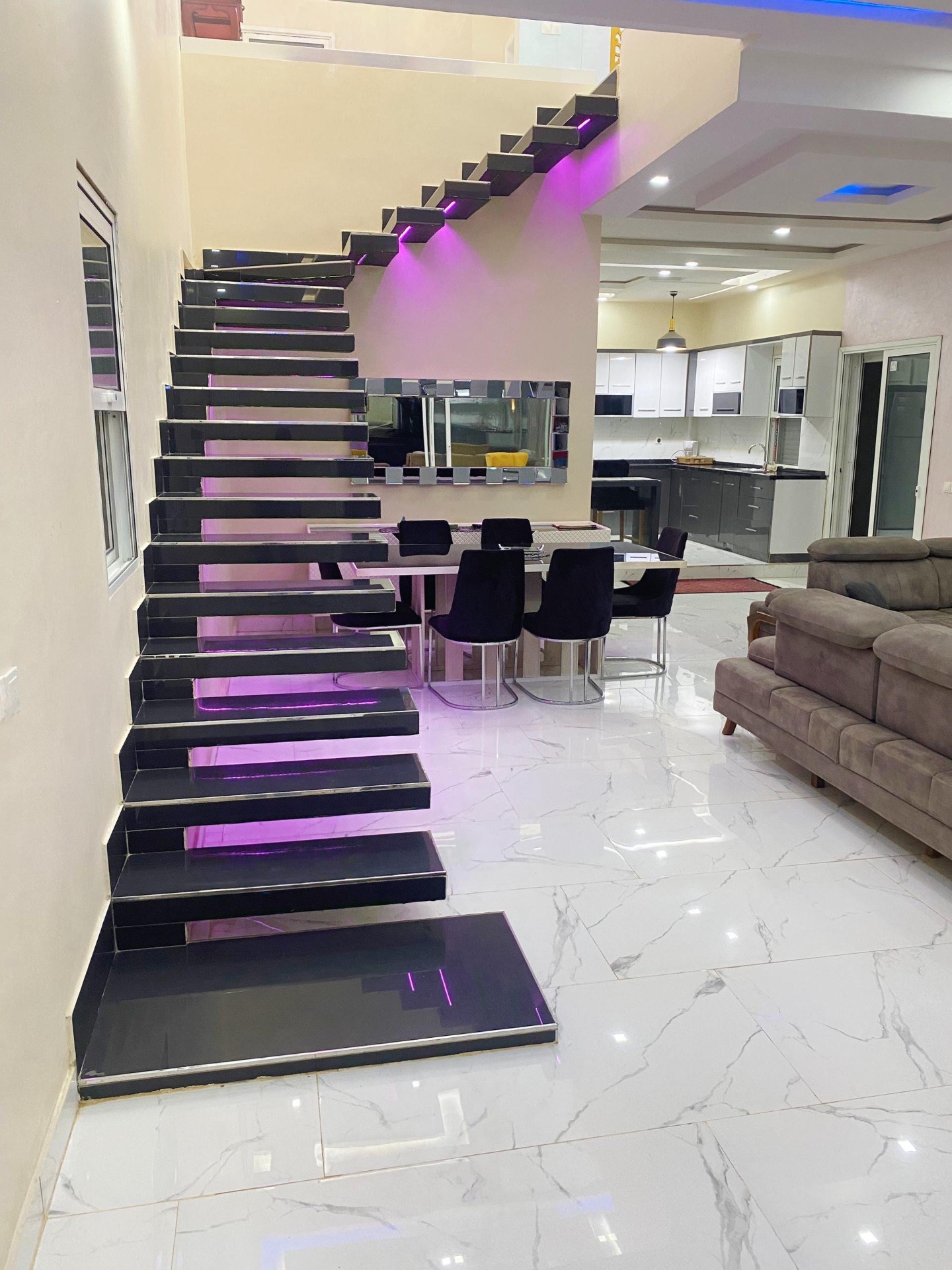 Salon ouvert avec escalier suspendu éclairé et cuisine moderne